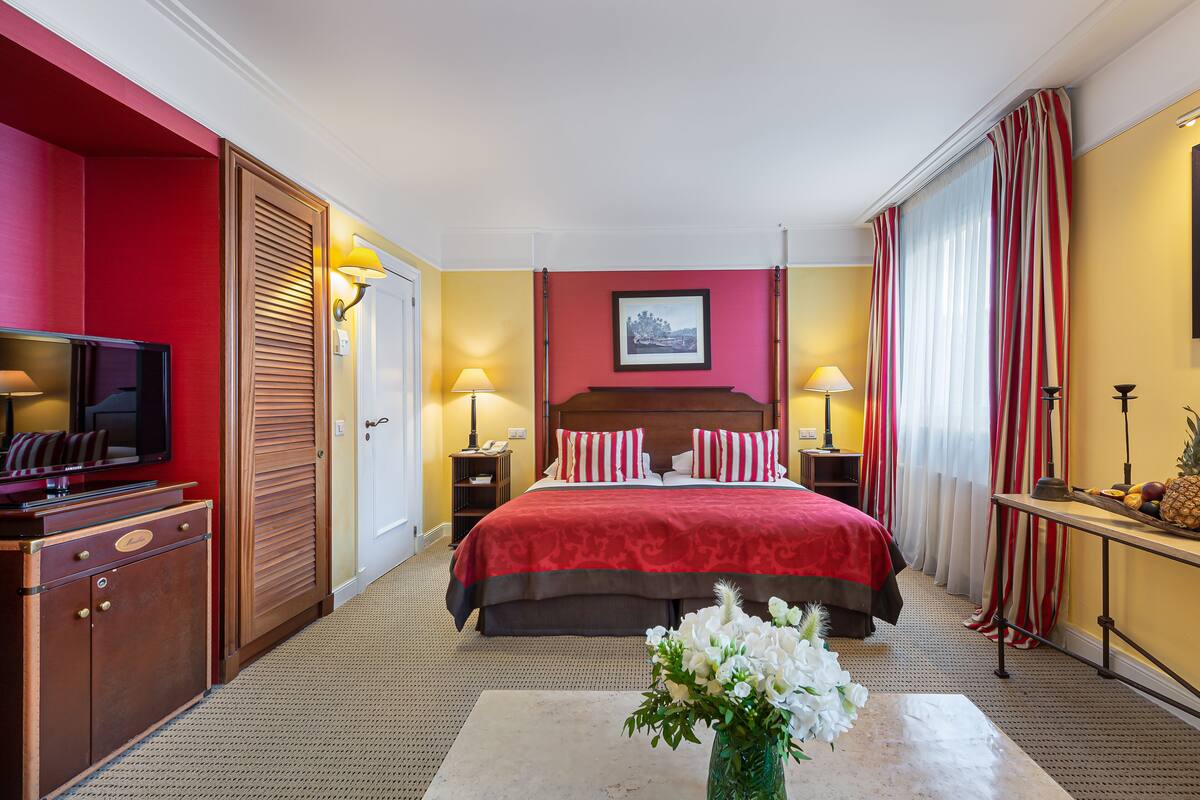 Een hotelkamer met een groot bed, een televisie, een bureau met een lamp en een bloemenvaas.