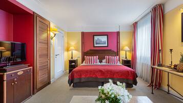 A hotel room with a large bed, a TV, a desk with a lamp, and a vase of flowers.