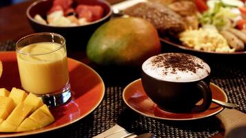 Un desayuno con vaso de jugo de naranja, taza de café con crema batida y diferentes platos que incluyen fruta y huevos.