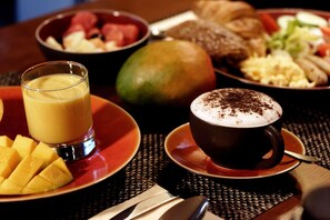 A breakfast setting with a glass of orange juice, a cup of coffee with whipped cream, and various dishes including fruit and eggs.