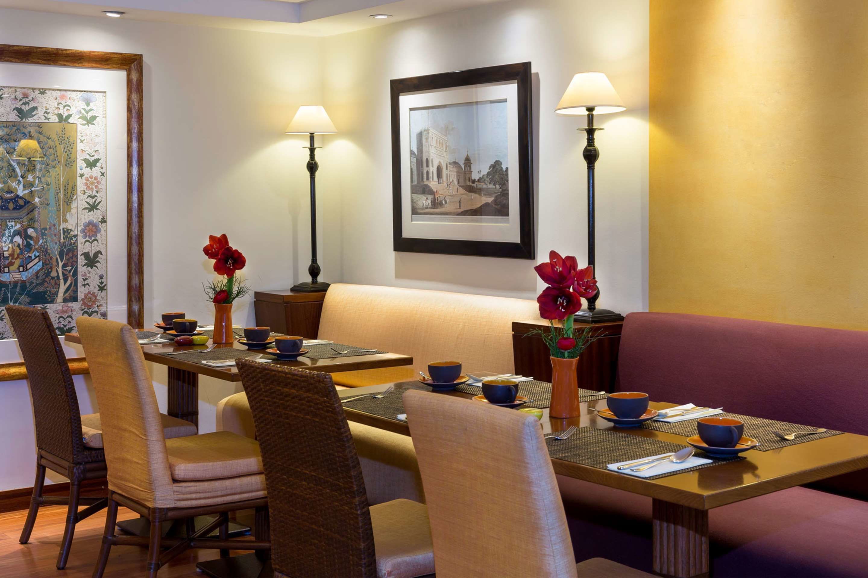 A dining area with a table set for two, surrounded by chairs, with a sofa and lamps in the background.