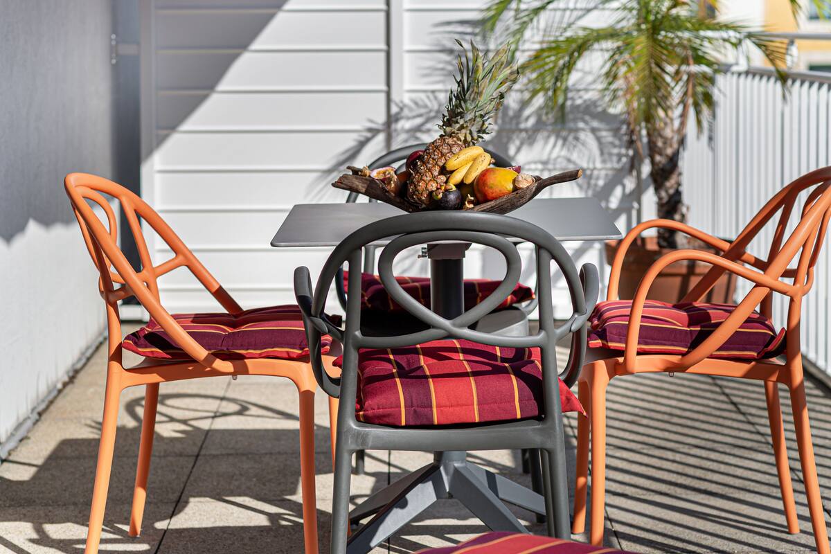 Een tafel met een fruitschaal, twee oranje stoelen met rode kussens, en een grijze tafel.