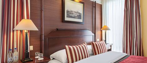 Une chambre d’hôtel avec un grand lit, deux tables de chevet, un tableau encadré au mur et des rideaux à rayures.