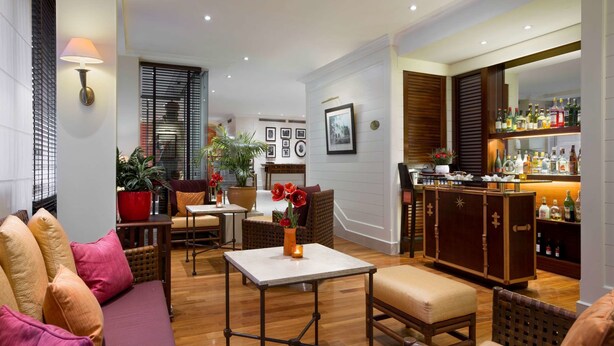 Una habitación de hotel acogedora con sofá, sillones, una pequeña mesa, zona de bar y planta en maceta.