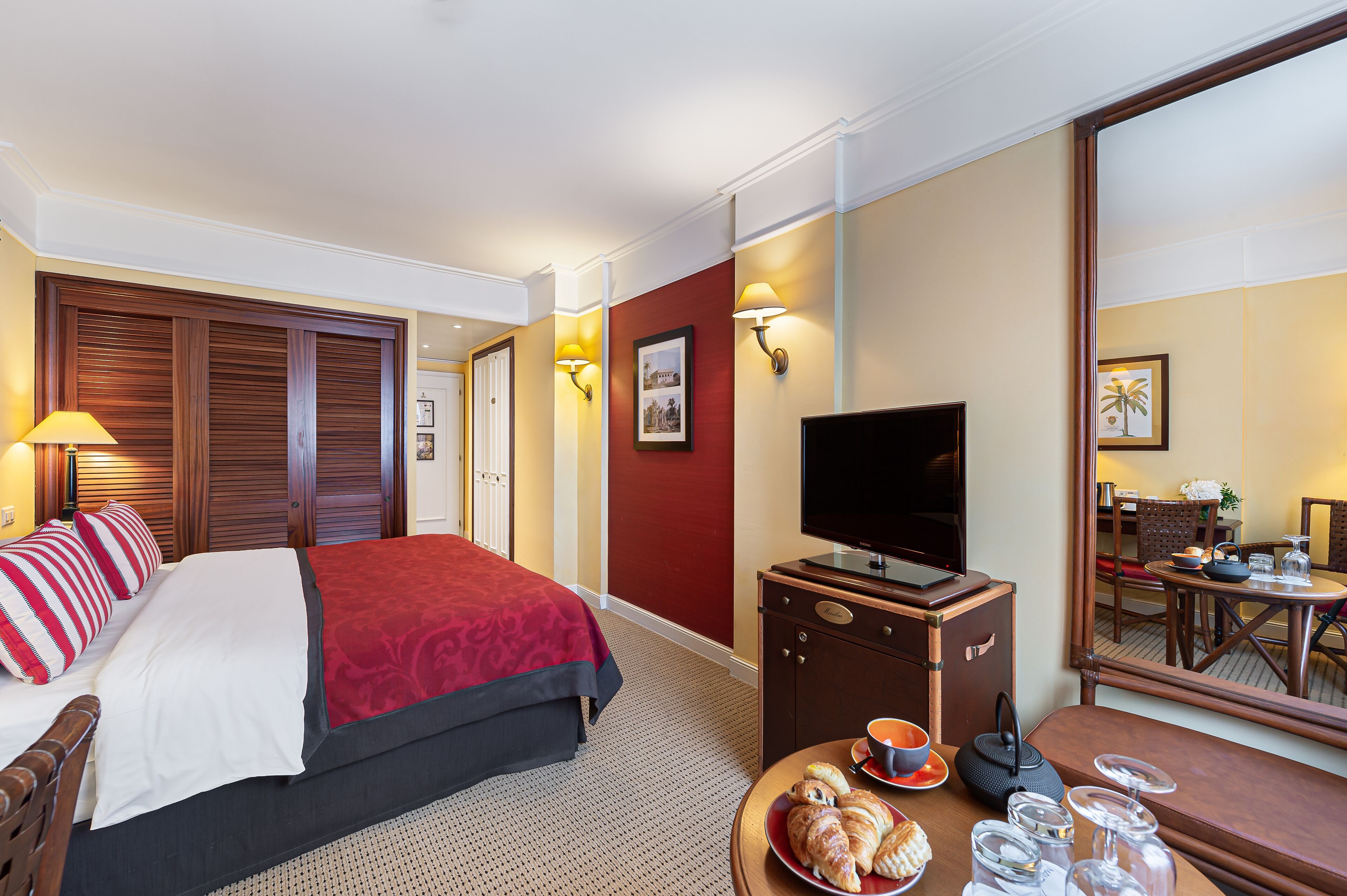 Quarto de hotel com uma cama, uma televisão, uma mesa de jantar com cadeiras e uma mesinha de centro.