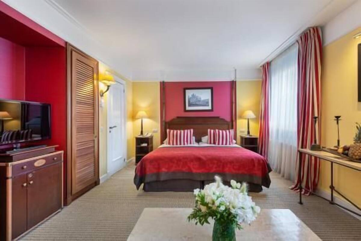 Een hotelkamer met een bed, een televisie, een bureau en een bloevas.