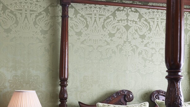 A four-poster bed with a wooden frame, a vase with flowers, and a bedside table with a lamp.