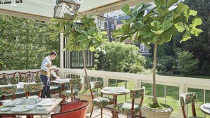 A restaurant with outdoor seating, tables, chairs, and a waiter.