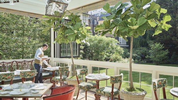 Un ristorante con posti a sedere all'aperto, tavoli, sedie e un cameriere.