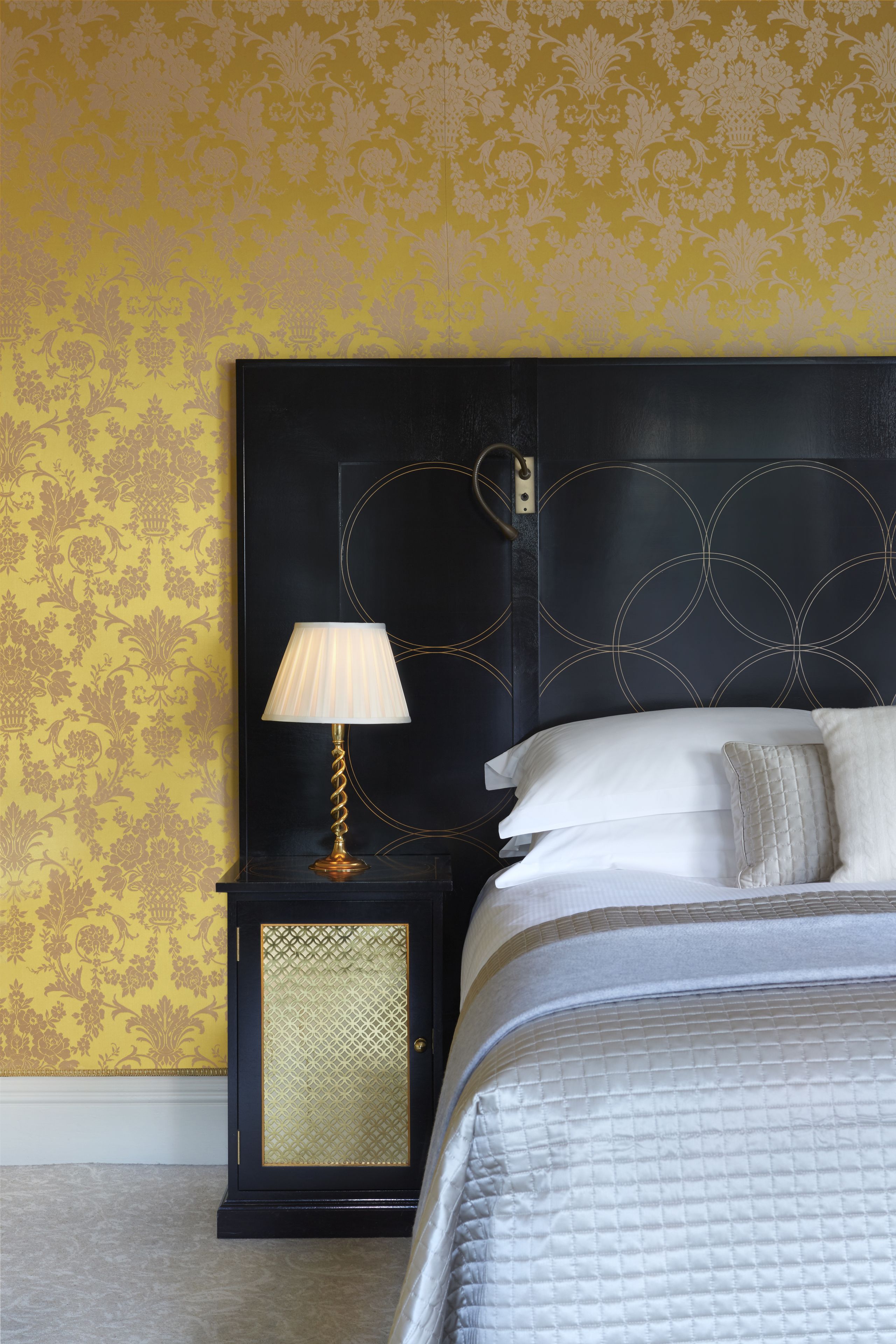 A bedroom with a bed, a nightstand, a lamp, and a wall with a floral pattern.