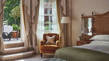 A bedroom with a bed, a green upholstered chair, a nightstand with a lamp, and a window with curtains.