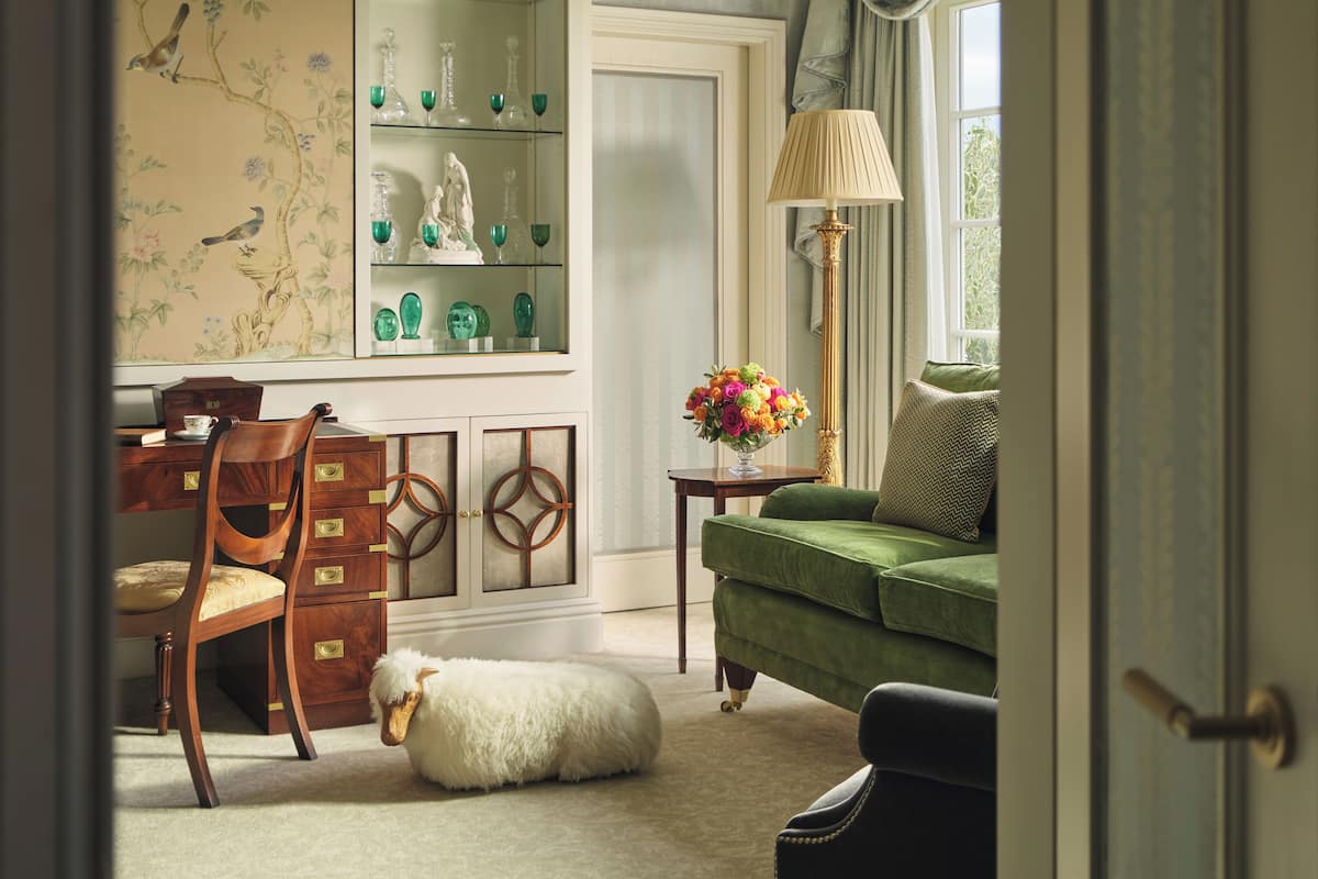 A room with a wooden desk, a green sofa, a lamp, and a decorative wall with a bird mural.
