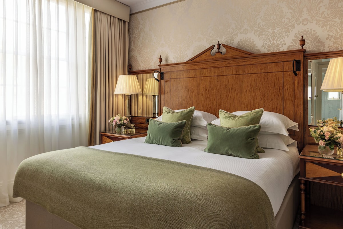A hotel room with a large bed, wooden headboard, two bedside tables with lamps, and a mirror.