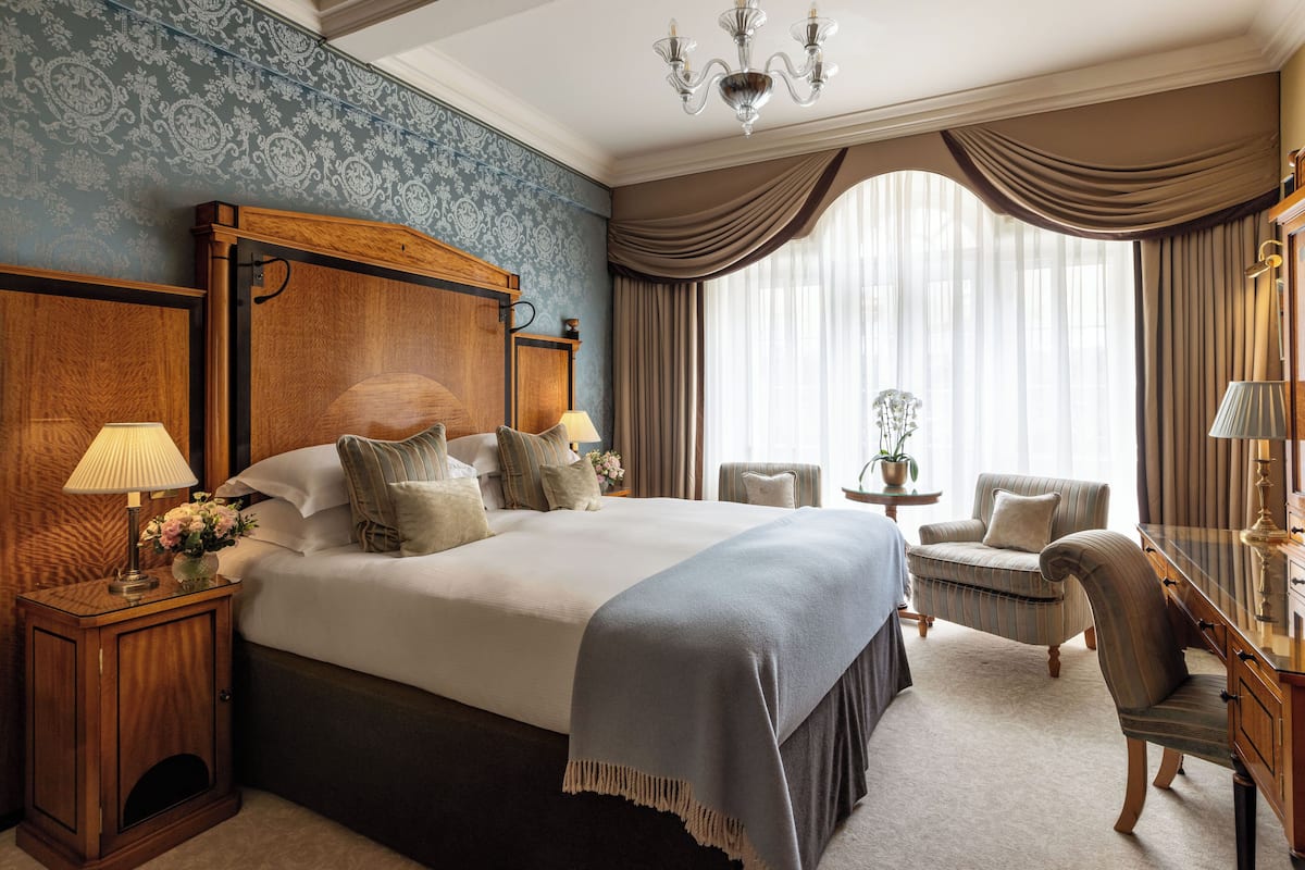 A large bed with a wooden headboard, two bedside tables with lamps, a chair, and a desk with a lamp.