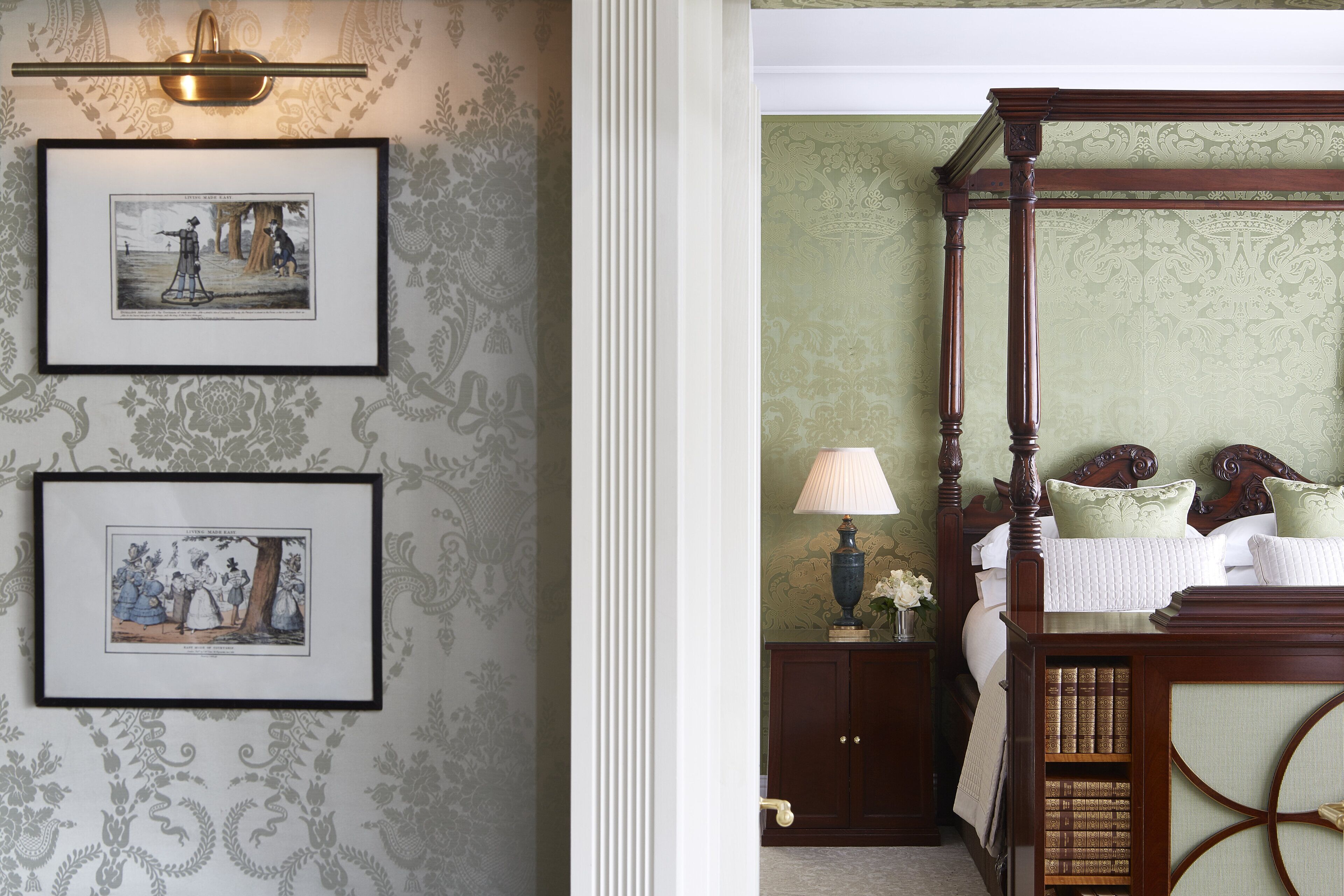 A bedroom with a four-poster bed, a nightstand with a lamp, and two framed pictures on the wall.
