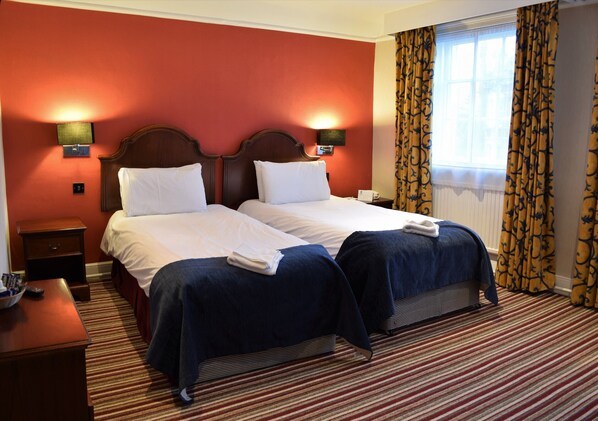 A hotel room with two beds, a nightstand with a lamp, and a window with curtains. - The Rose and Crown Hotel – Tonbridge (Tonbridge)