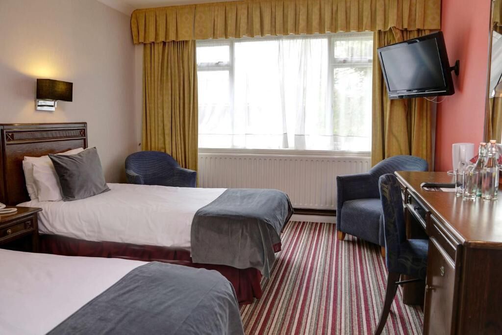 Une chambre d’hôtel avec deux lits, un bureau, une chaise, une télévision et une fenêtre avec des rideaux.