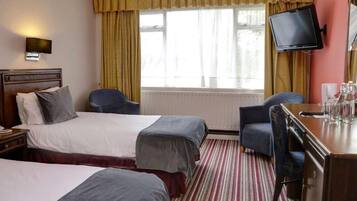 Une chambre d’hôtel avec deux lits, un bureau, une chaise, une télévision et une fenêtre avec des rideaux.