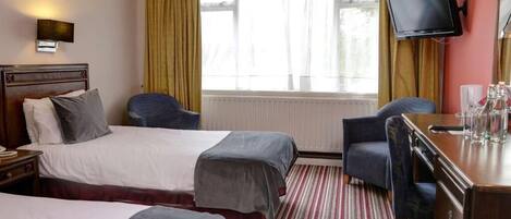 A hotel room with two beds, a desk, a chair, a television, and a window with curtains.