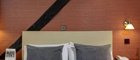 Habitación de hotel con una cama grande, vigas de madera, una mesita de noche con lámpara y un teléfono en la pared.