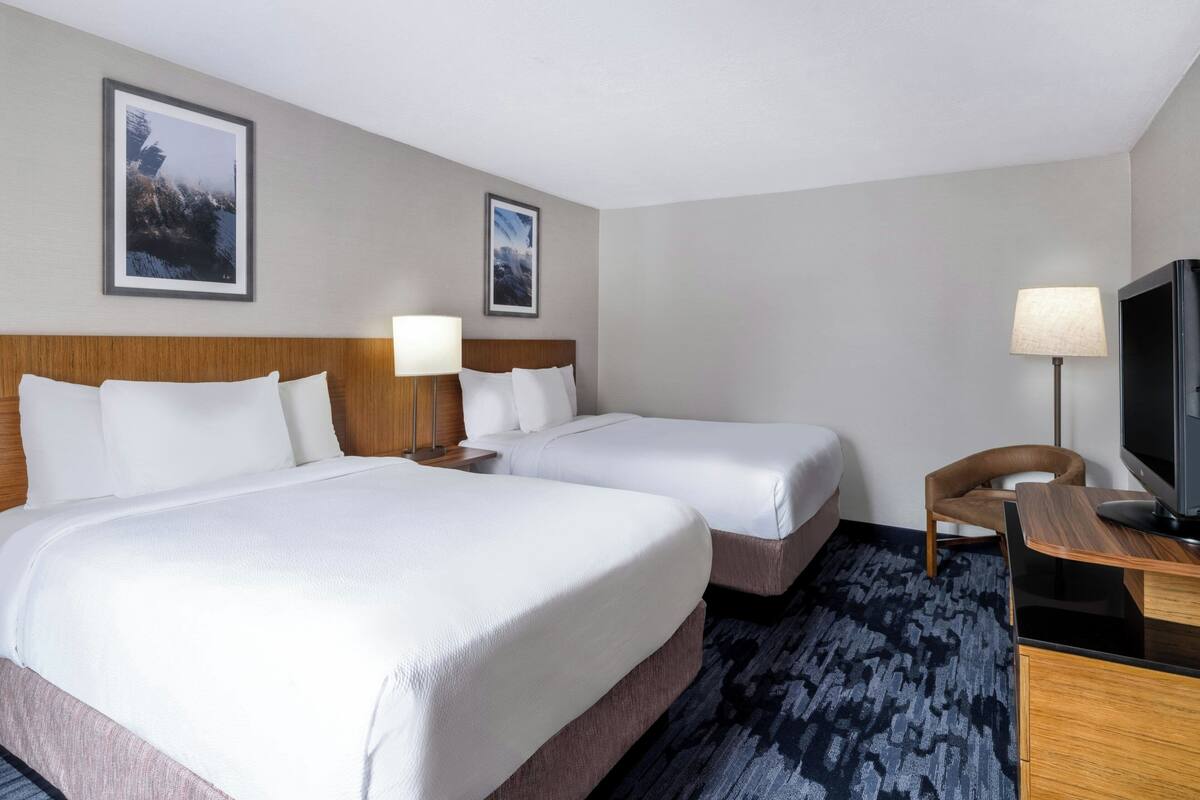 A hotel room with two beds, a desk, a chair, a TV, and two framed pictures on the wall.