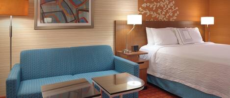 Habitación de hotel con sofá azul, una mesita, cama con ropa de cama blanca y dos lámparas de noche.