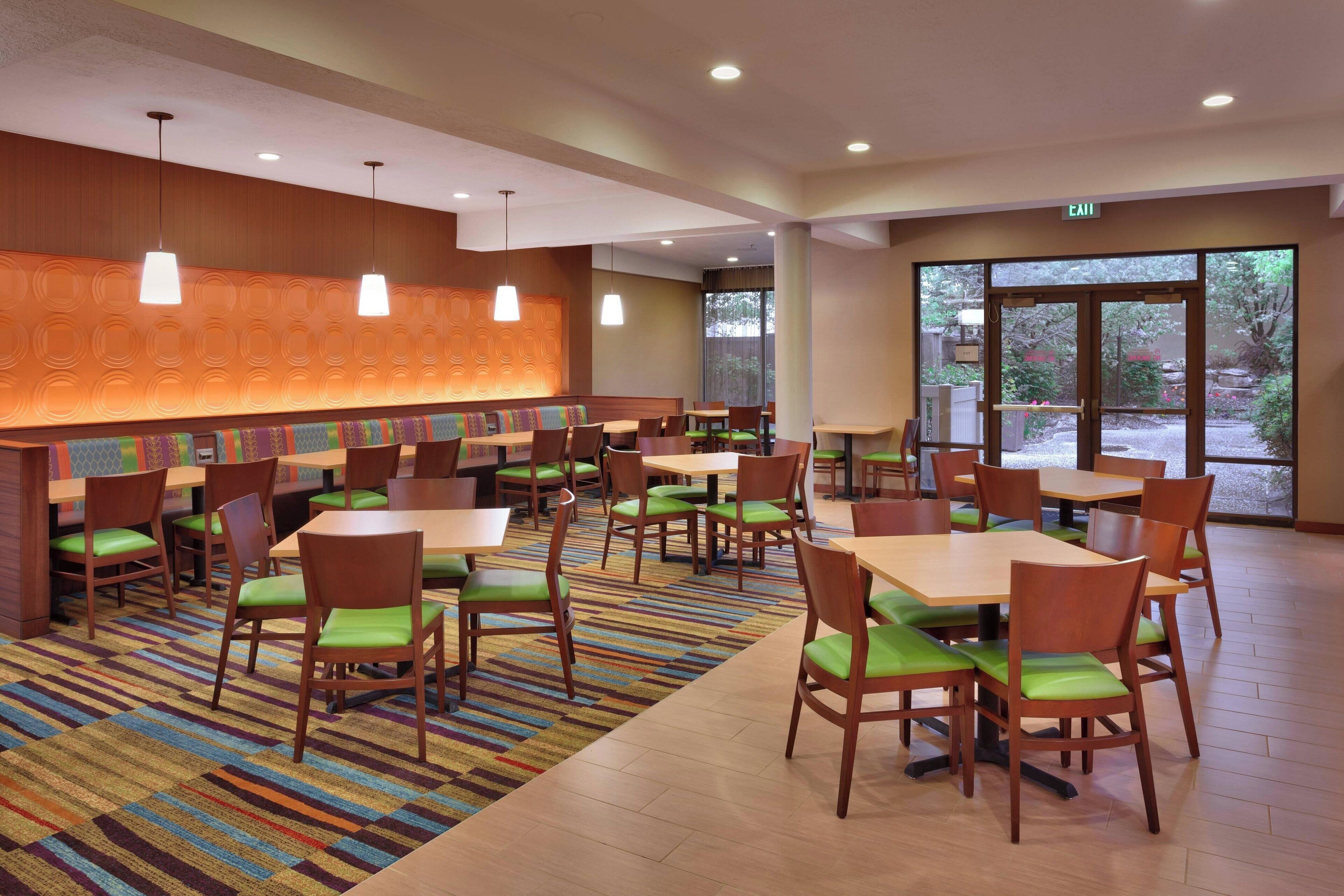 A spacious dining area with multiple tables and chairs, a patterned wall, and a large window providing natural light.