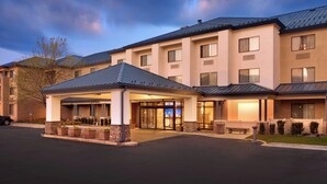 A multi-story hotel with a covered entrance, outdoor seating, and a parking lot.