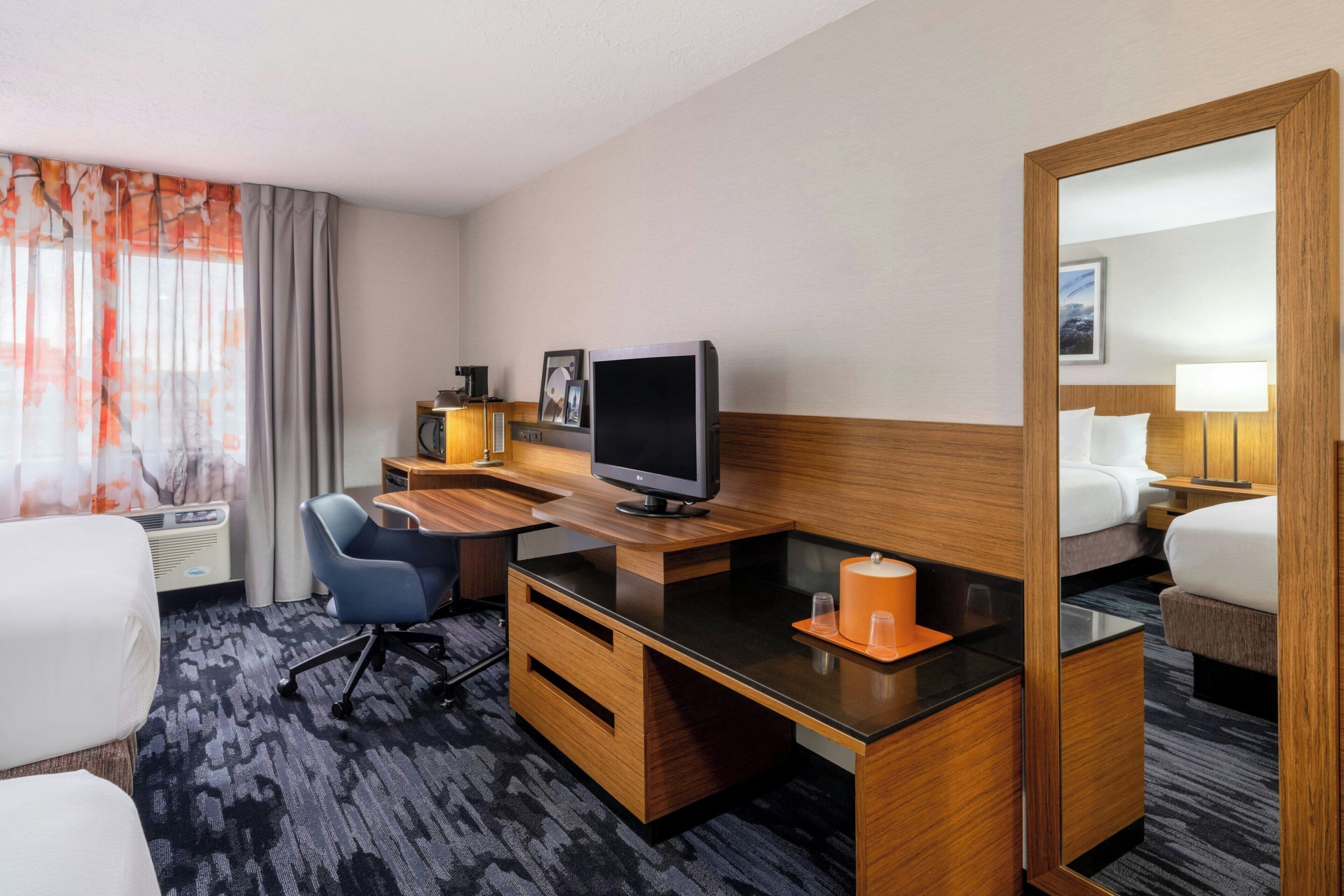 Una habitación de hotel con escritorio, televisión, silla, cama y un espejo grande.