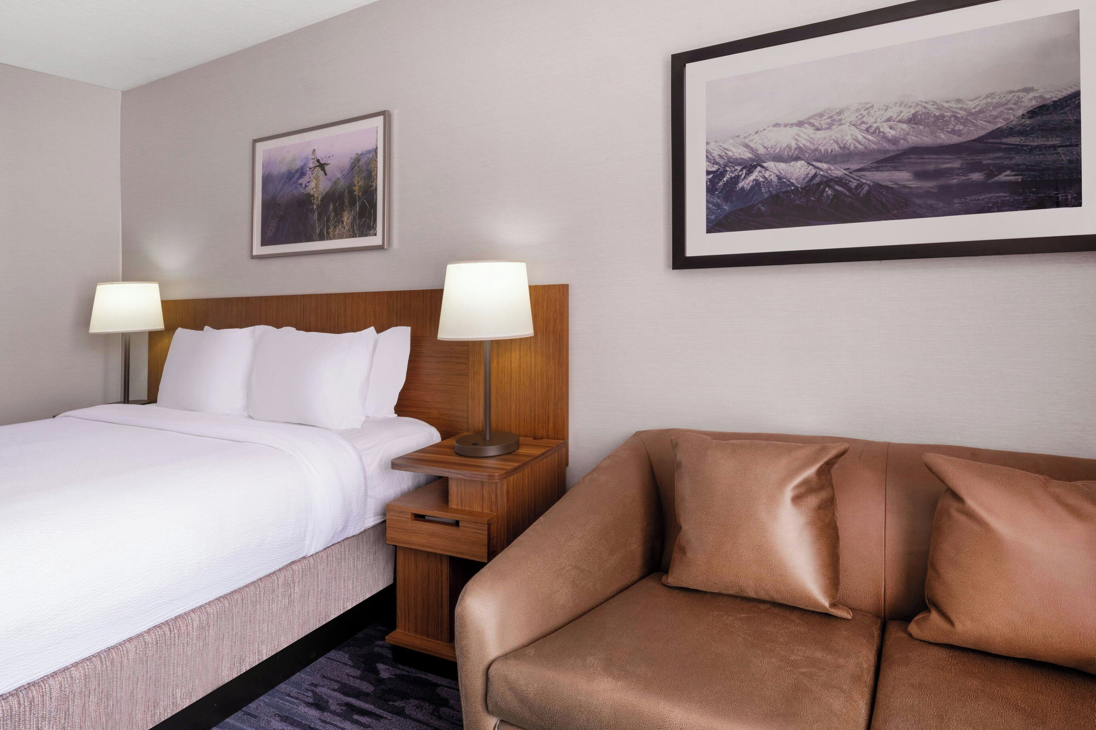 Ein Hotelzimmer mit einem Bett, Nachttischen, einem Sofa und zwei gerahmten Bildern an der Wand.