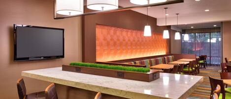 A hotel lobby with a marble reception desk, leather seating, a flat-screen TV, a wall-mounted light fixture, and a patterned carpet.
