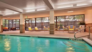 An indoor swimming pool with clear water, surrounded by yellow and brown lounge chairs, and large windows offering views of the outside.