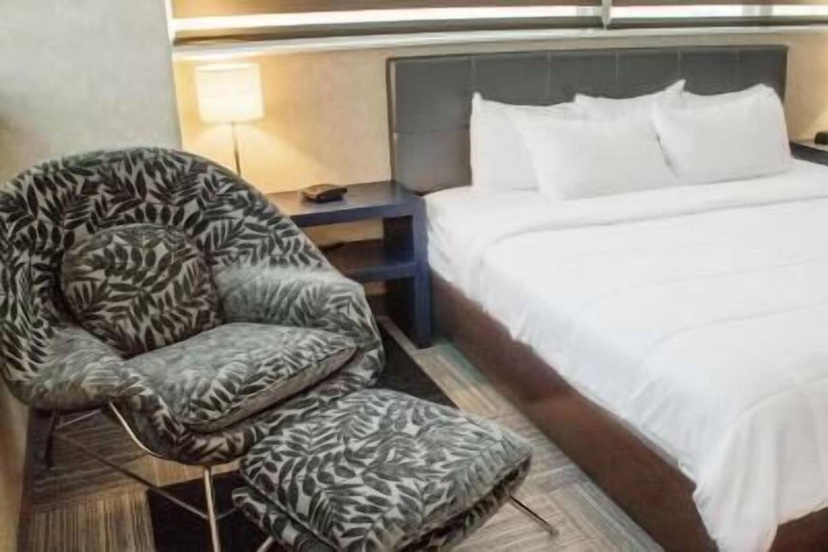 Une chambre d’hôtel avec un lit, une chaise, une table de chevet et une lampe.
