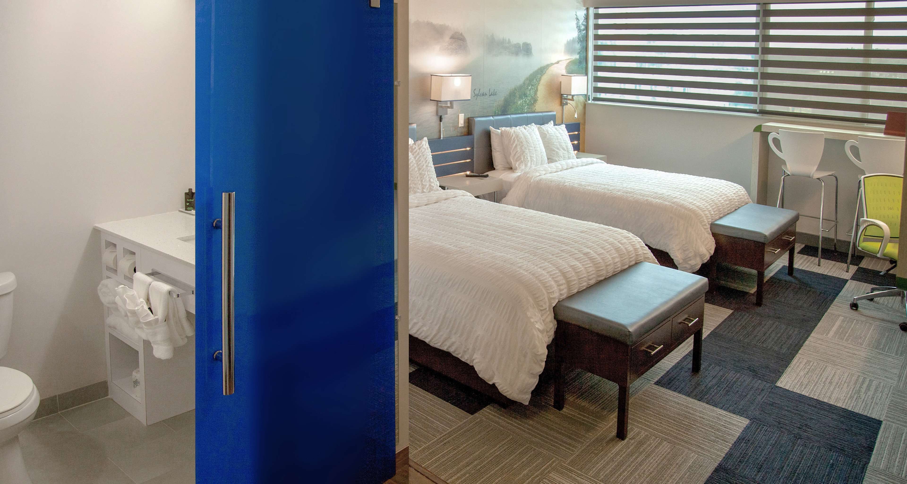 Habitación de hotel con dos camas, baño, escritorio y ventana con persianas.