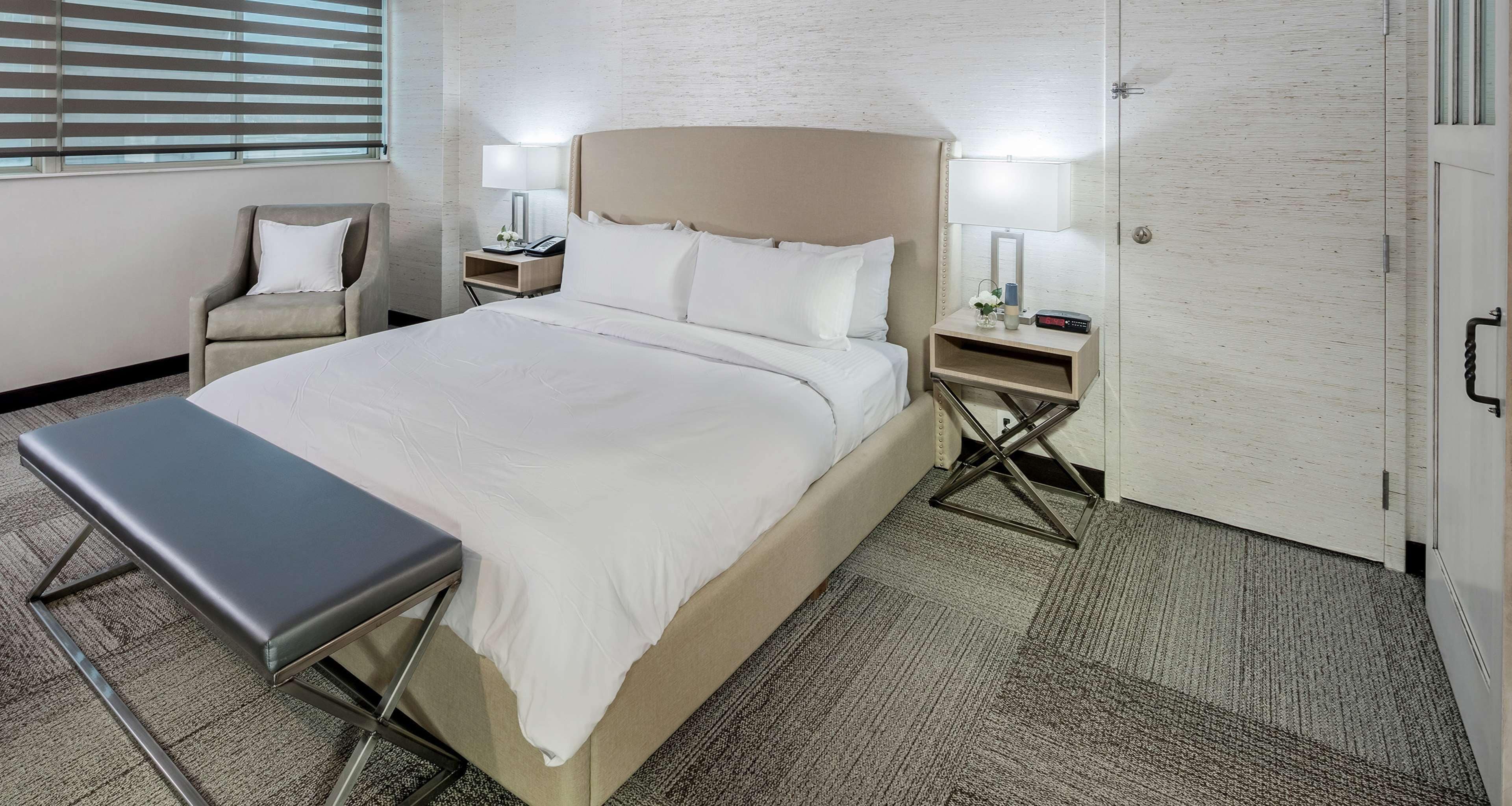A hotel room with a large bed, bedside tables, a chair, and a bench.