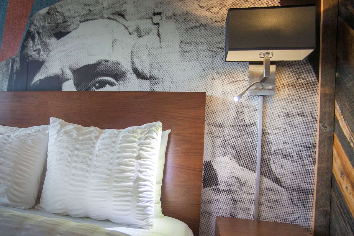 Une chambre d’hôtel avec un grand lit, une tête de lit, une fresque murale, une table de chevet et une lampe.