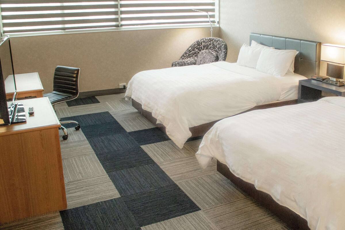 Une chambre d’hôtel avec deux lits, un bureau, une chaise et une lampe.