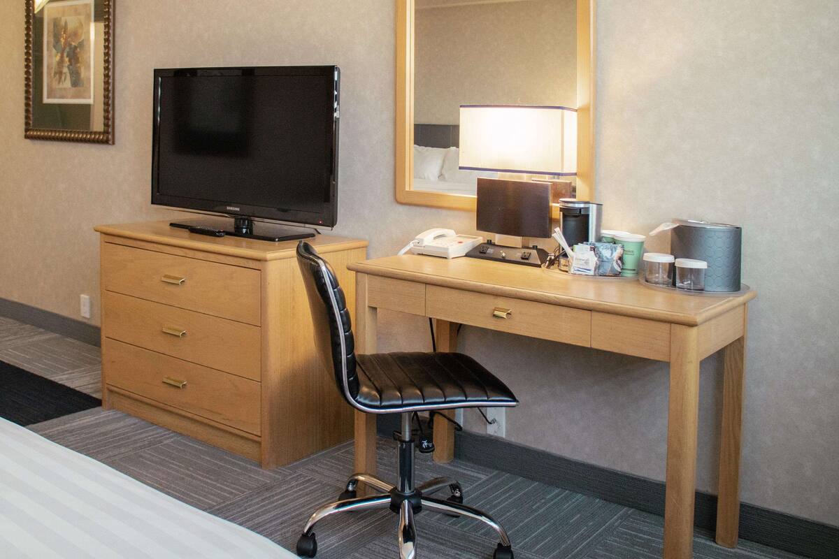 Une chambre d’hôtel équipée d’un lit, d’un bureau avec un ordinateur, d’une chaise, d’une télévision, d’un téléphone et d’une machine à café.