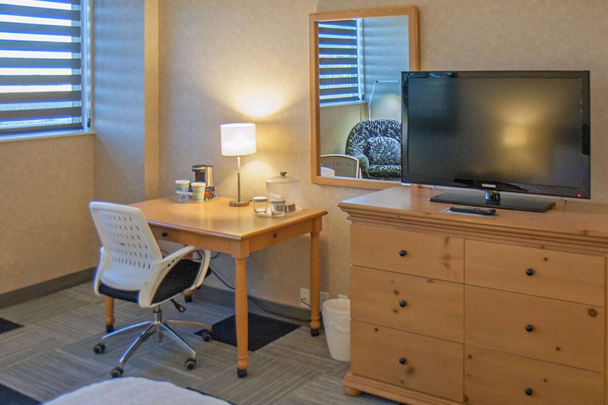 Une chambre d’hôtel avec un bureau en bois, une chaise, une télévision, une commode et un miroir.