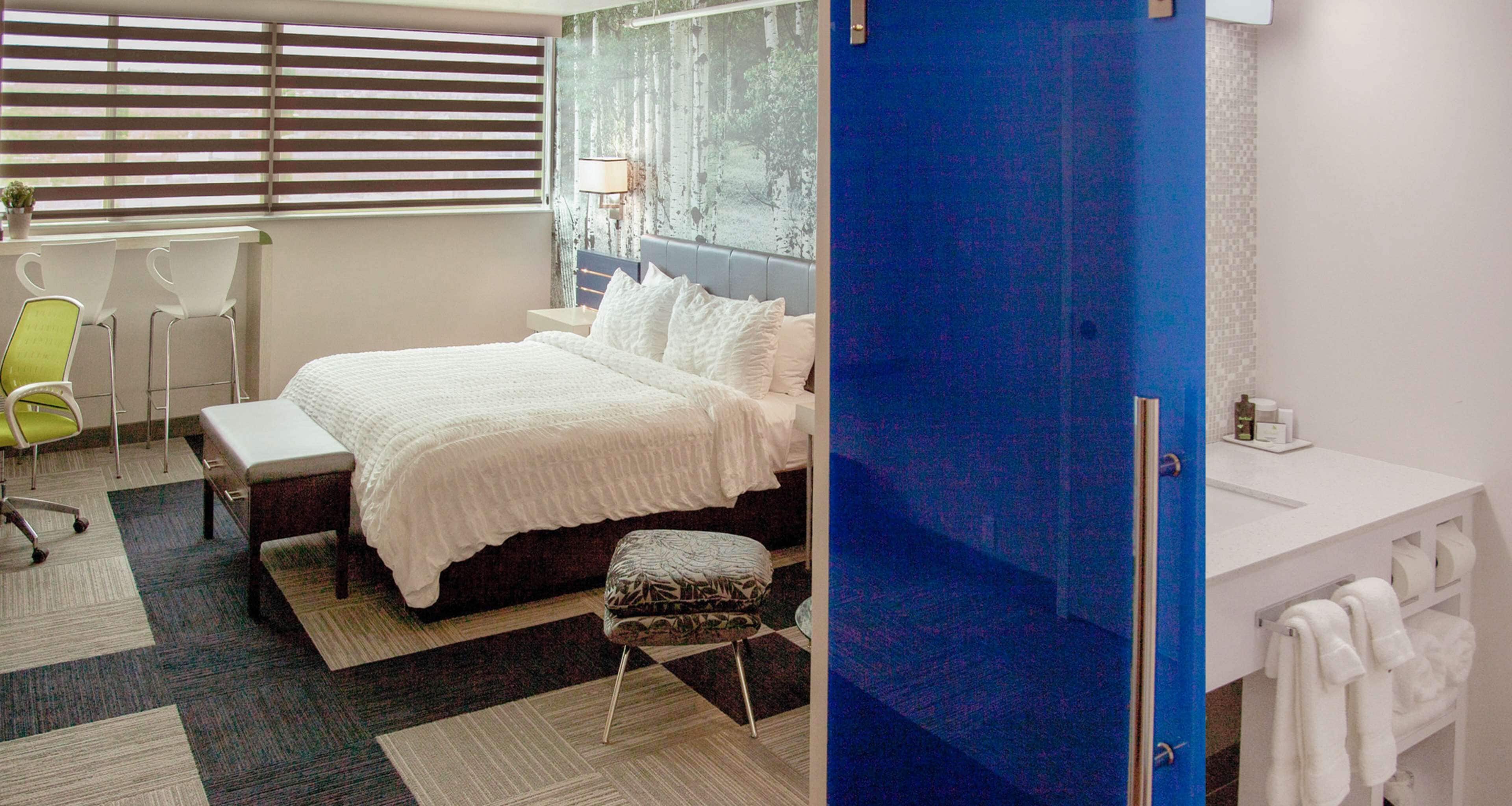 Une chambre d’hôtel avec un lit, un bureau, une chaise et une salle de bain équipée d’un lavabo et de serviettes.