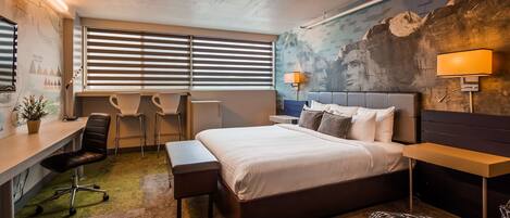 Ett modernt hotellrum med en stor säng, ett skrivbord, två stolar, en bänk och en väggmålning.
