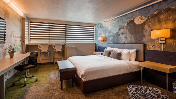 Ein modernes Hotelzimmer mit einem großen Bett, einem Schreibtisch, zwei Stühlen, einer Bank und einem Wandgemälde.