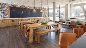 Um café moderno com mesas e bancos de madeira, grandes janelas e uma parede de tijolos.