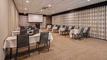 A conference room with multiple tables and chairs, a projector screen, and a patterned curtain wall.