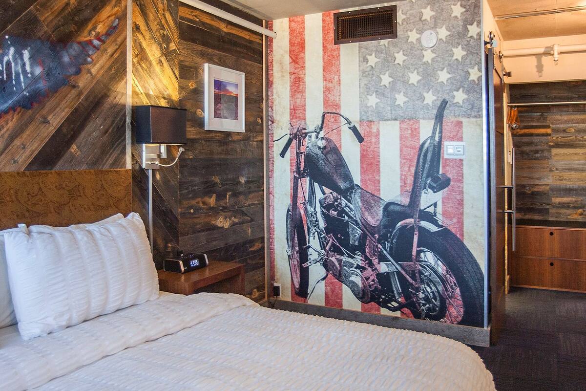 Une chambre d’hôtel avec un lit, une horloge murale, un tableau encadré et une fresque représentant une moto.