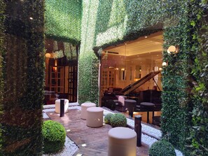 Un exuberante jardín interior con una terraza de madera, zonas de estar y una escalera que lleva a un nivel superior.