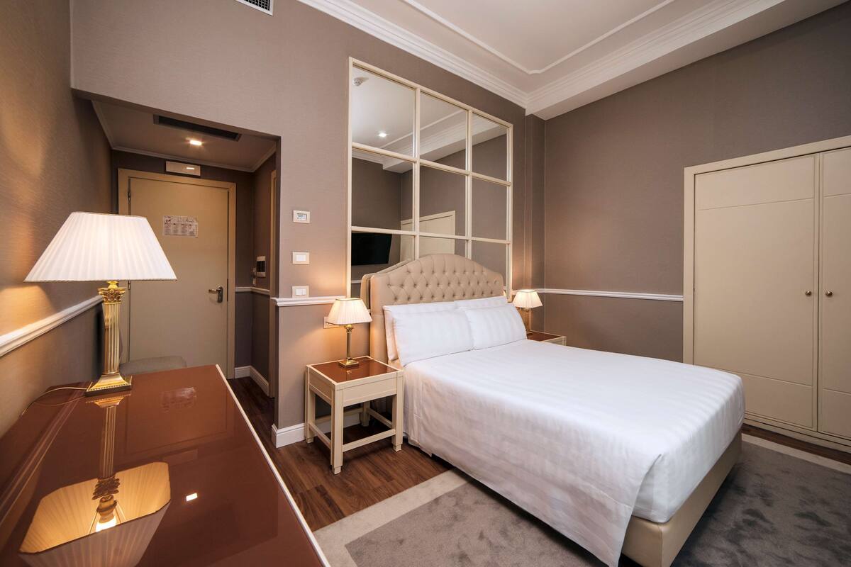 A hotel room with a large bed, two bedside tables with lamps, a wardrobe, and a mirror.