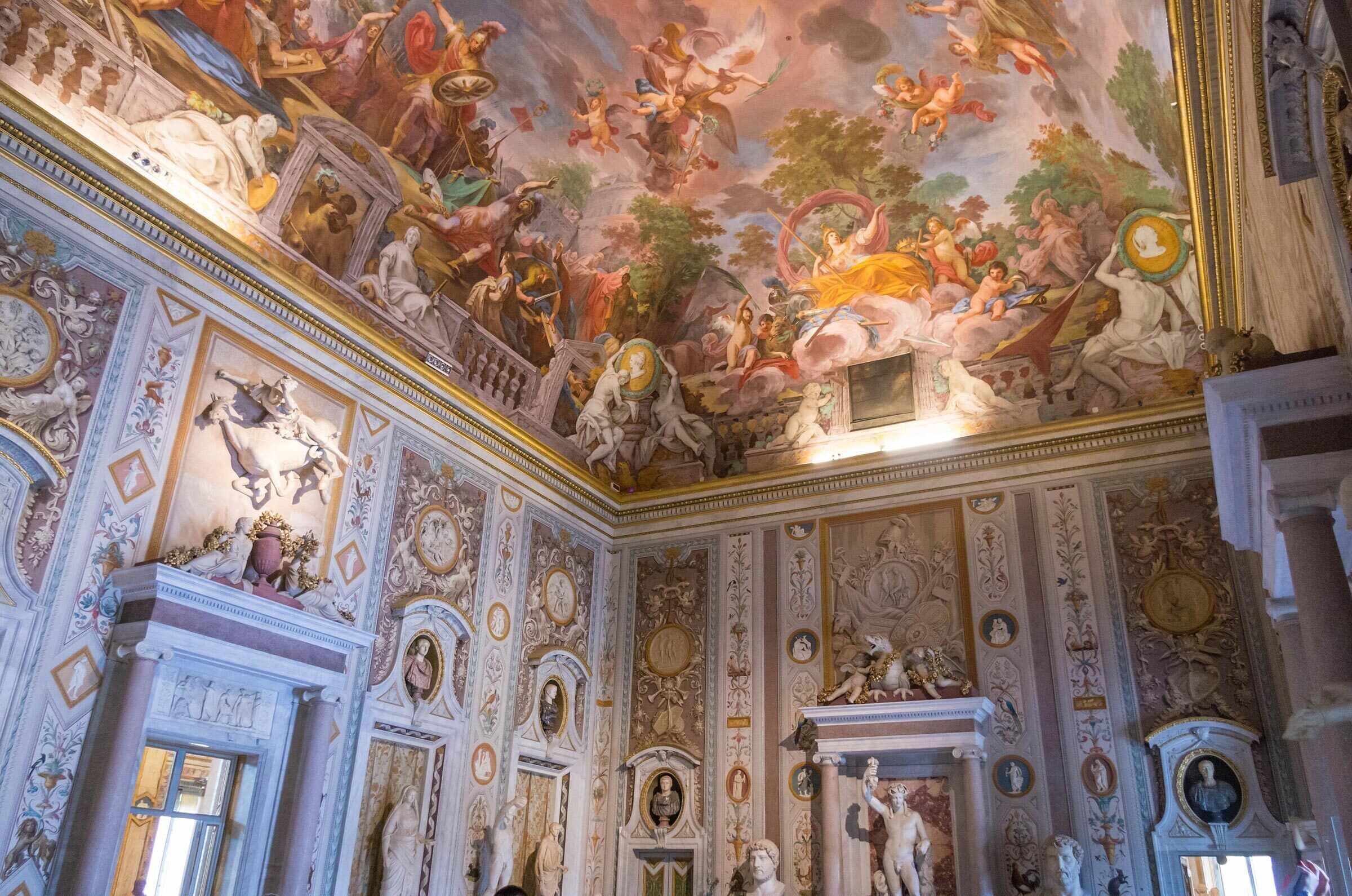 A grand hall with ornate ceiling frescoes and classical statues.