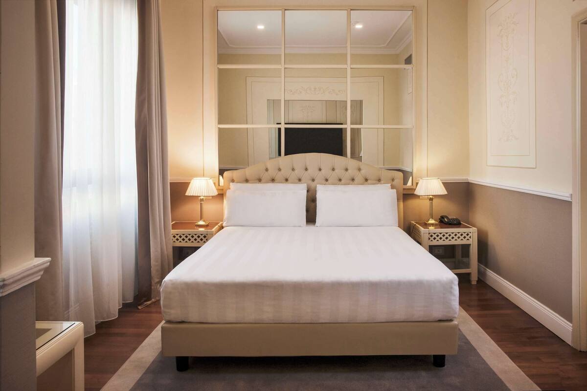 A neatly made bed with a tufted headboard, two bedside tables with lamps, and a large mirror above the bed.