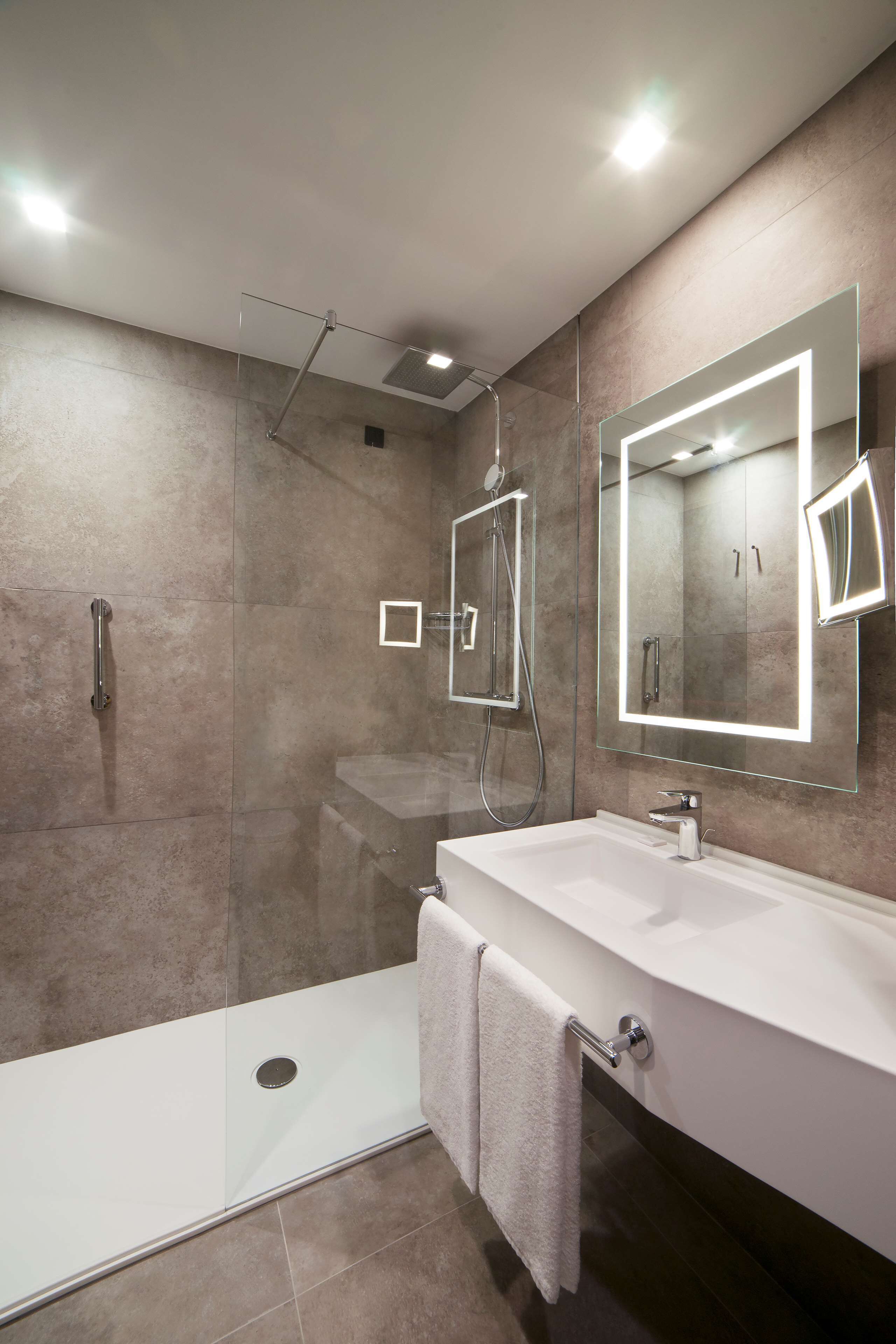 Un baño moderno con ducha de vidrio, un espejo grande y un lavamanos blanco.